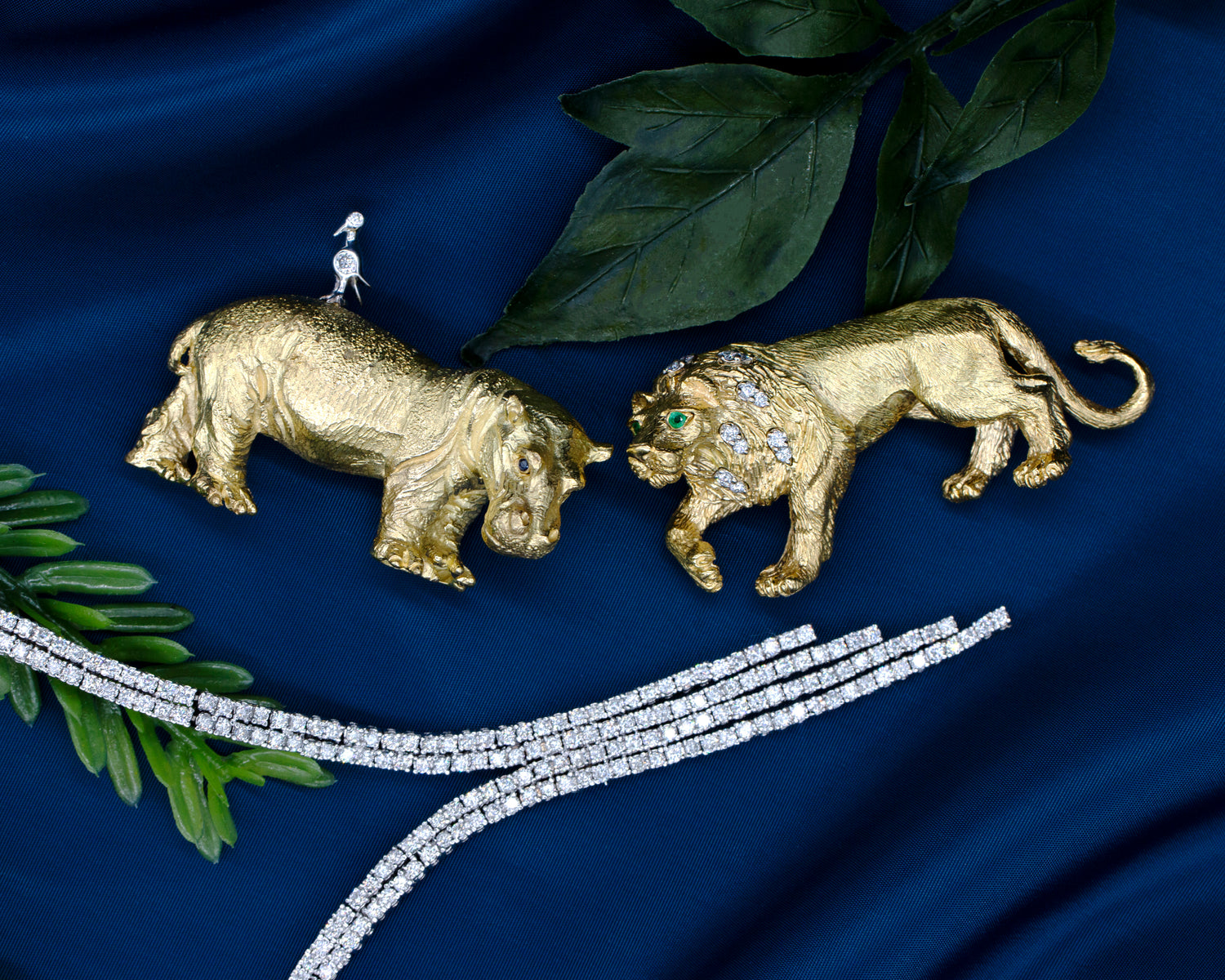 Photo featuring yellow gold vintage Tiffany's hippo and lion brooches featuring diamonds, sapphires, and emeralds. As well as a white gold diamonds necklace on a blue silk background.